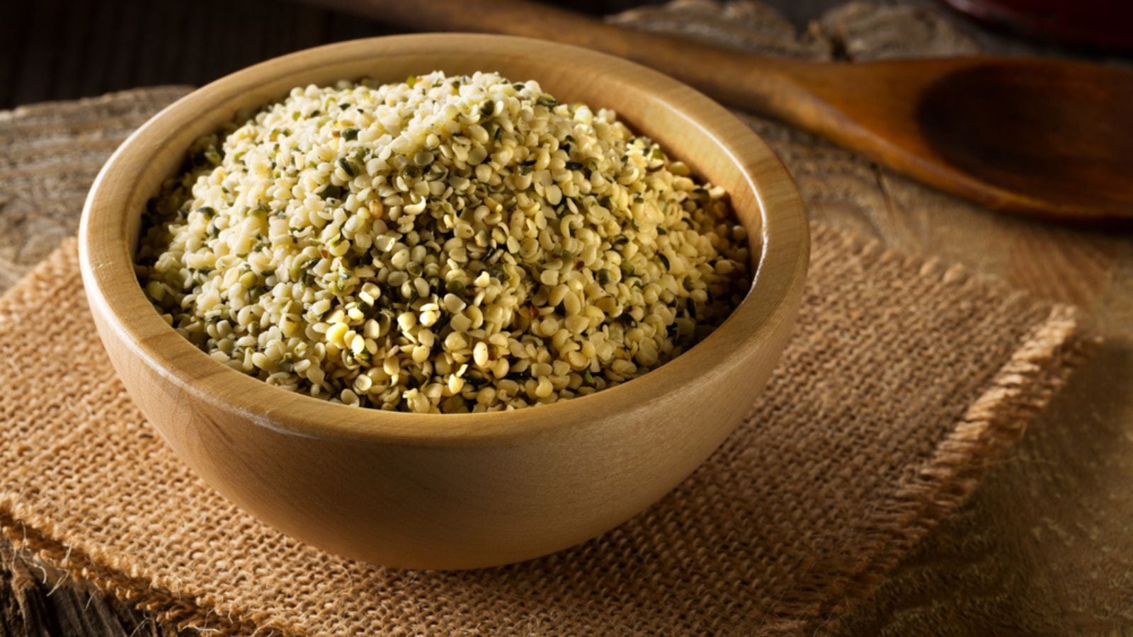 Heap of raw, organic hemp seeds in wooden bowl on burlap on rustic table background
