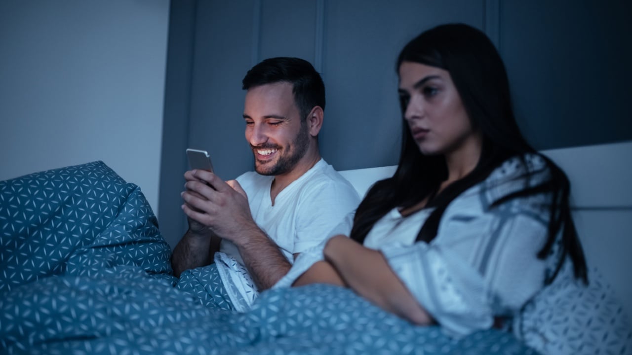 Young couple in the bedroom at night. Man using his mobile phone.