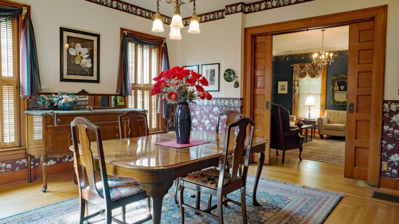 Dayton, Ohio, USA - June 10, 2018: Victorian dining room with wallpaper, high ceiling, silver chandelier, oriential rug & Queen Anne table, chairs & buffet in old home with pocket doors.