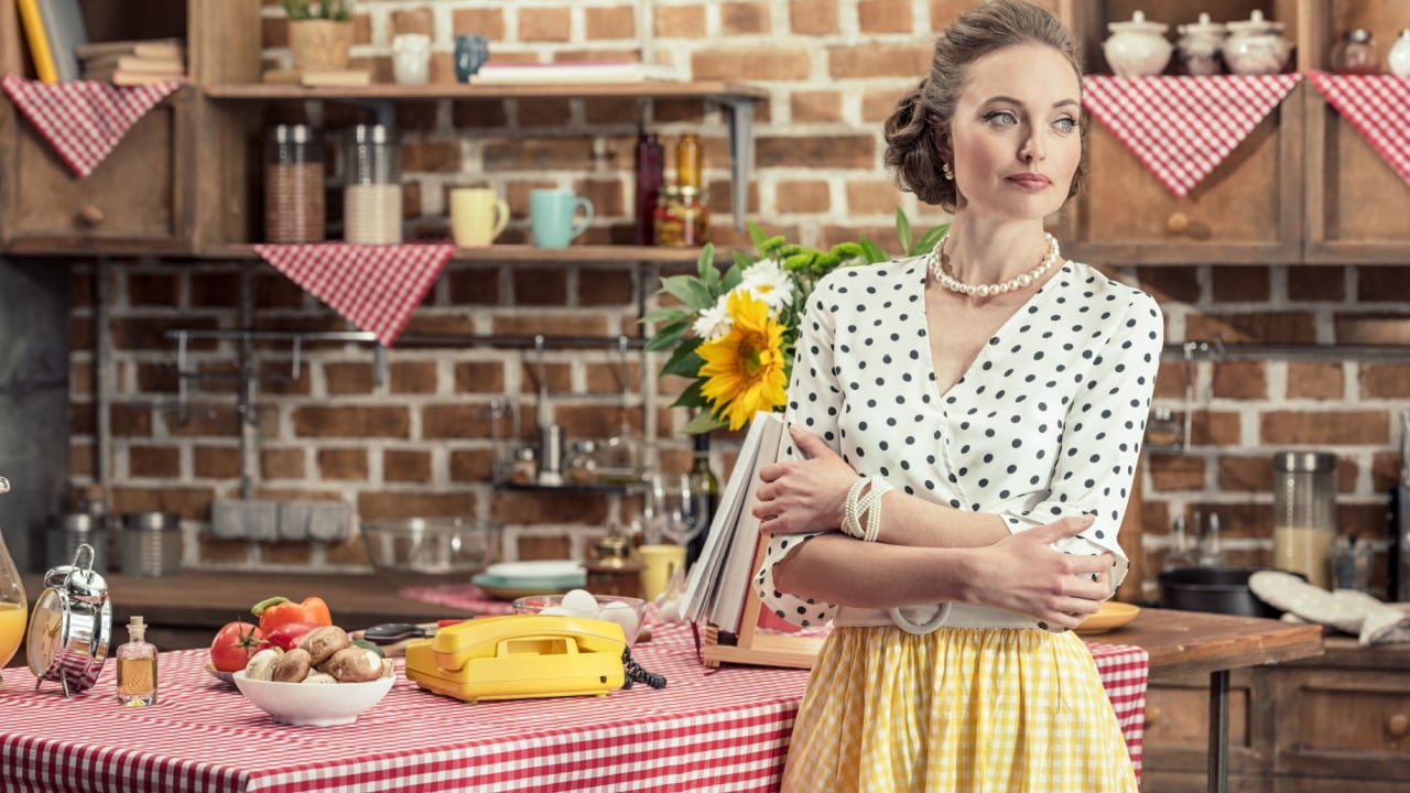 serious adult housewife in vintage clothes looking away at kitchen