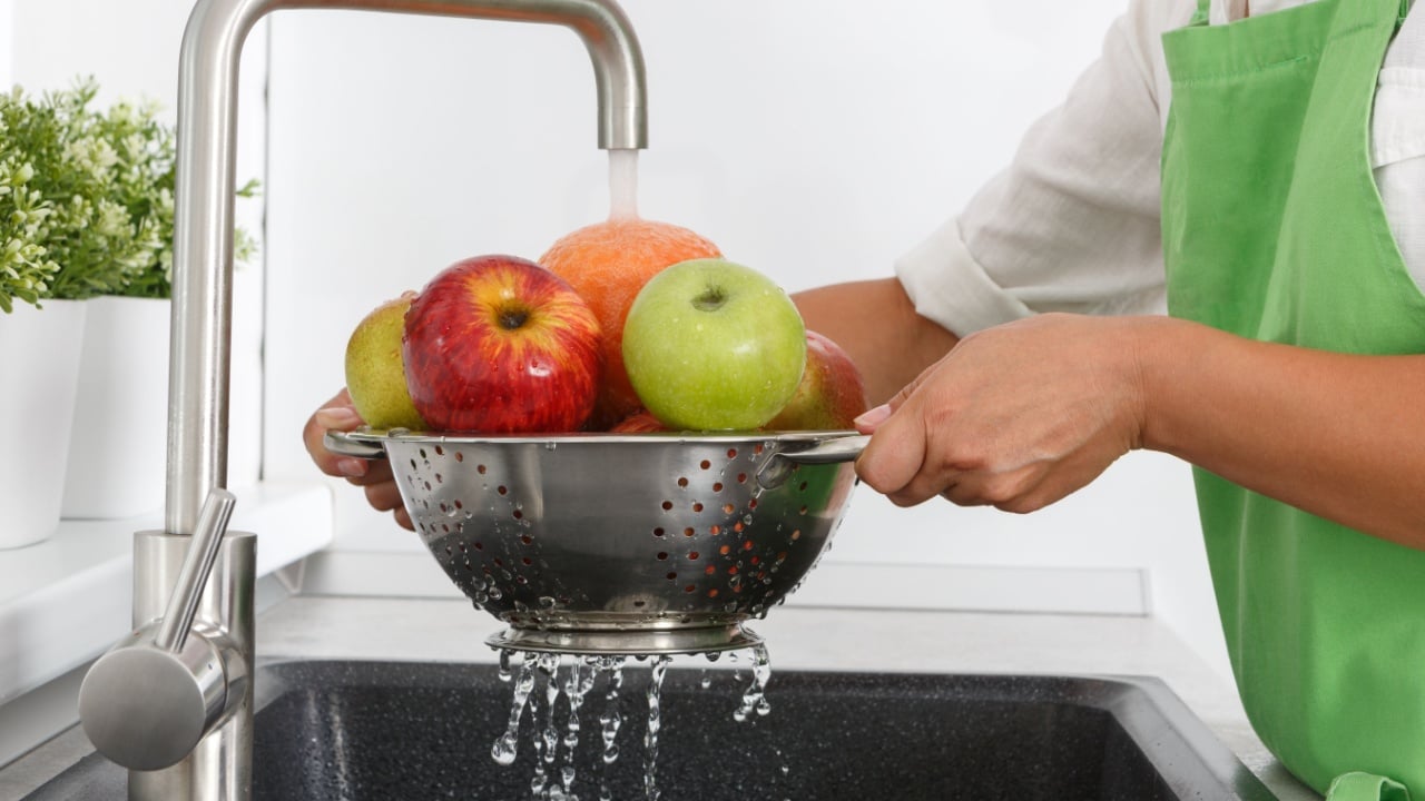 Cook woman washes fruits under running water from a water tap.