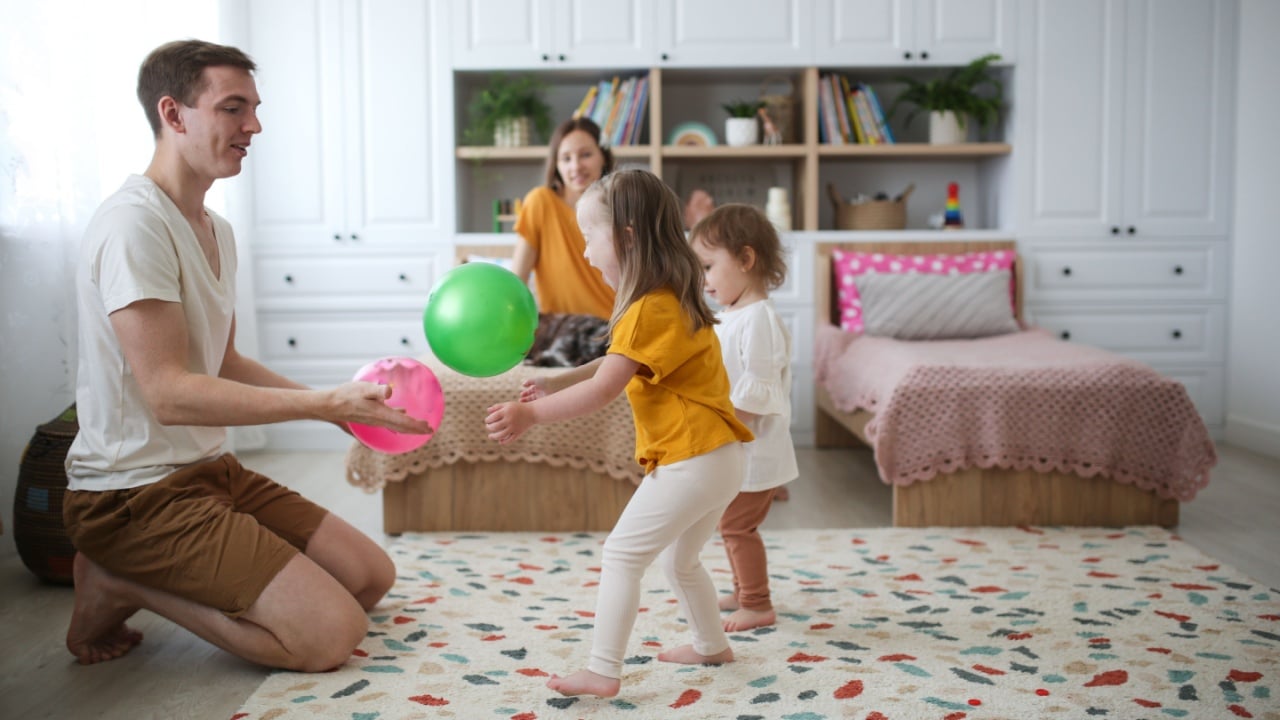 Beautiful Caucasian family playing with balls at home in the nursery, two daughters playing ball with their parents. A girl with Down syndrome and a sister play with their parents. Bright interior