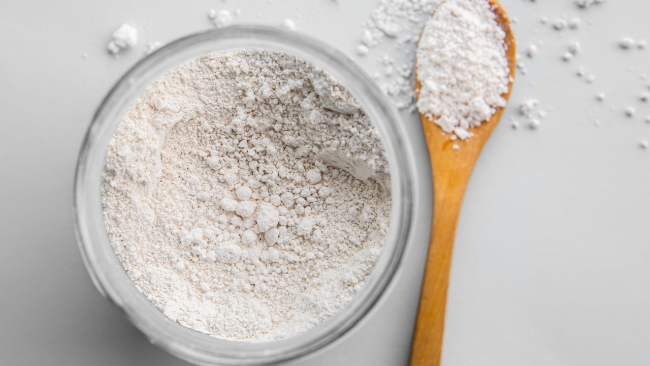 Diatomaceous earth also known as diatomite mixed in glass jar and wood spoon on gray background, studio shot. Detox ingredient.