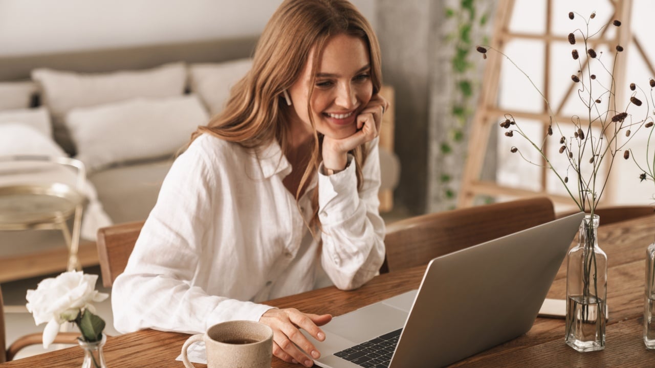 Image of young pleased happy cheerful cute beautiful business woman sit indoors in office using laptop computer listening music with earphones.