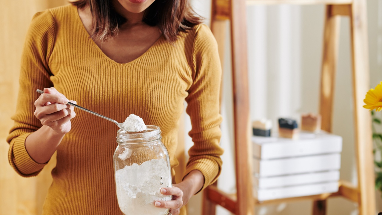 Smiling young woman taking spoon of soda lye from glass jar when making fragrant soap at home