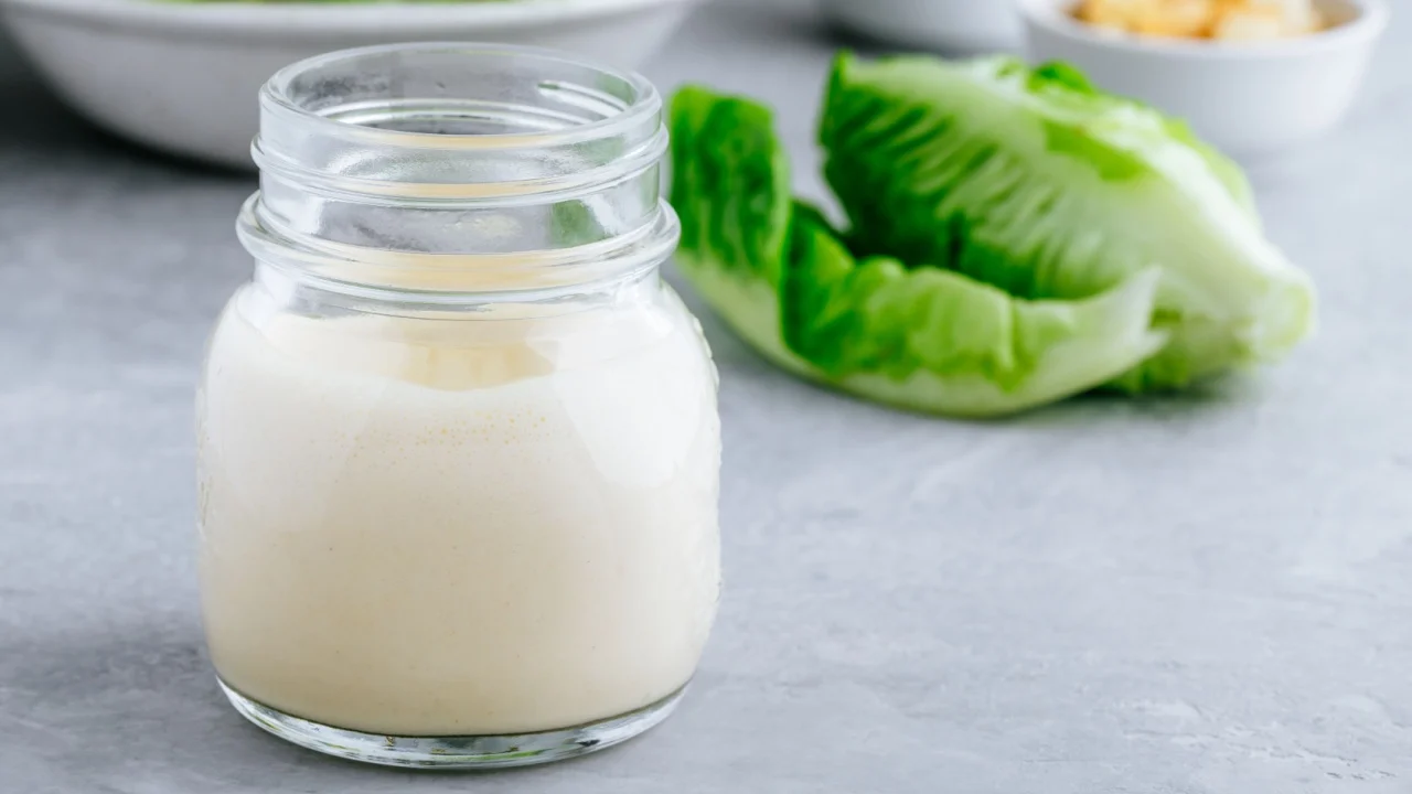 Homemade Caesar Salad Dressing in glass jar on gray stone background