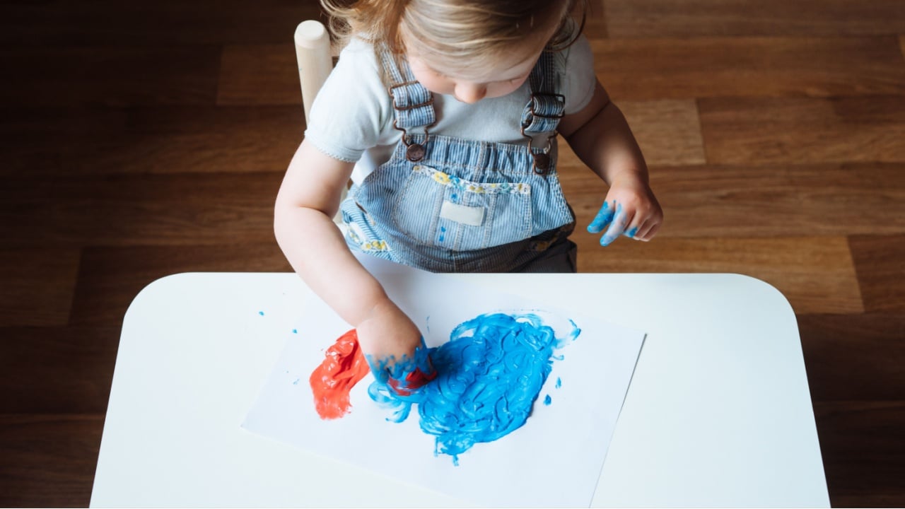 Child painting with her hands on the table at home using blue and red paint. Finger painting or art therapy for children. Fun activities for toddlers. 