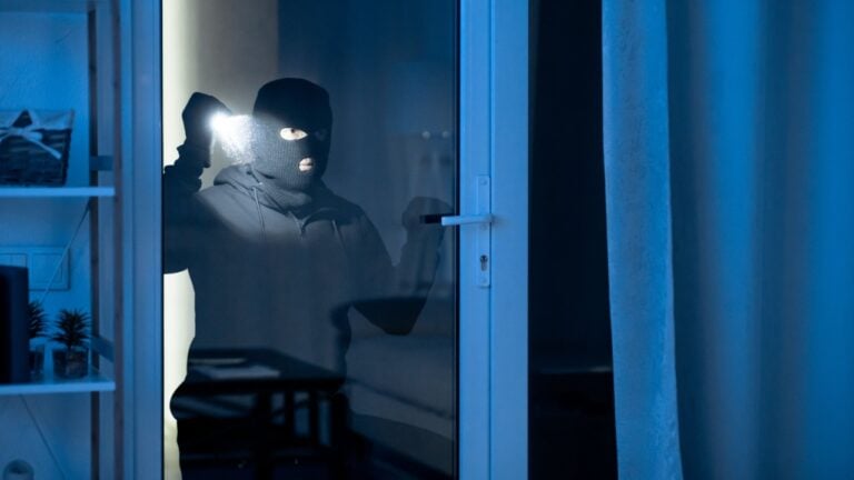 Criminal Act Concept. Portrait of robber checking apartment through balcony door, using flashlight torch.