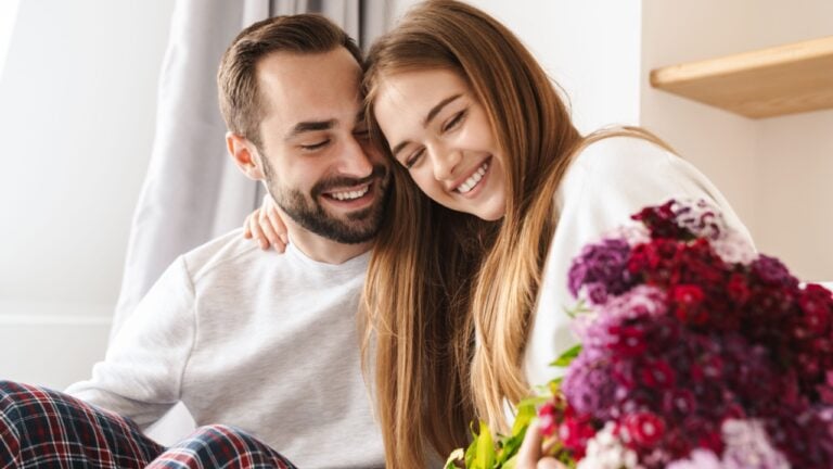 Happy man giving his lovely girlfriend bouquet of flowers while she is laying in bed
