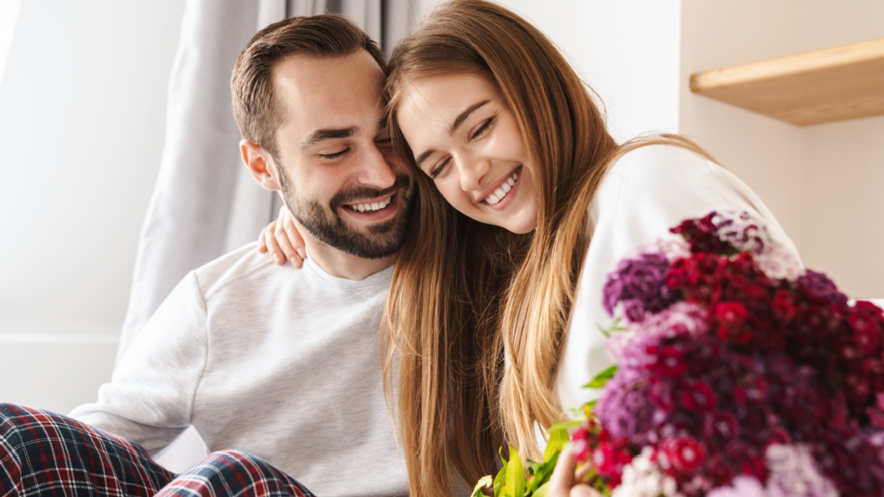 Happy man giving his lovely girlfriend bouquet of flowers while she is laying in bed