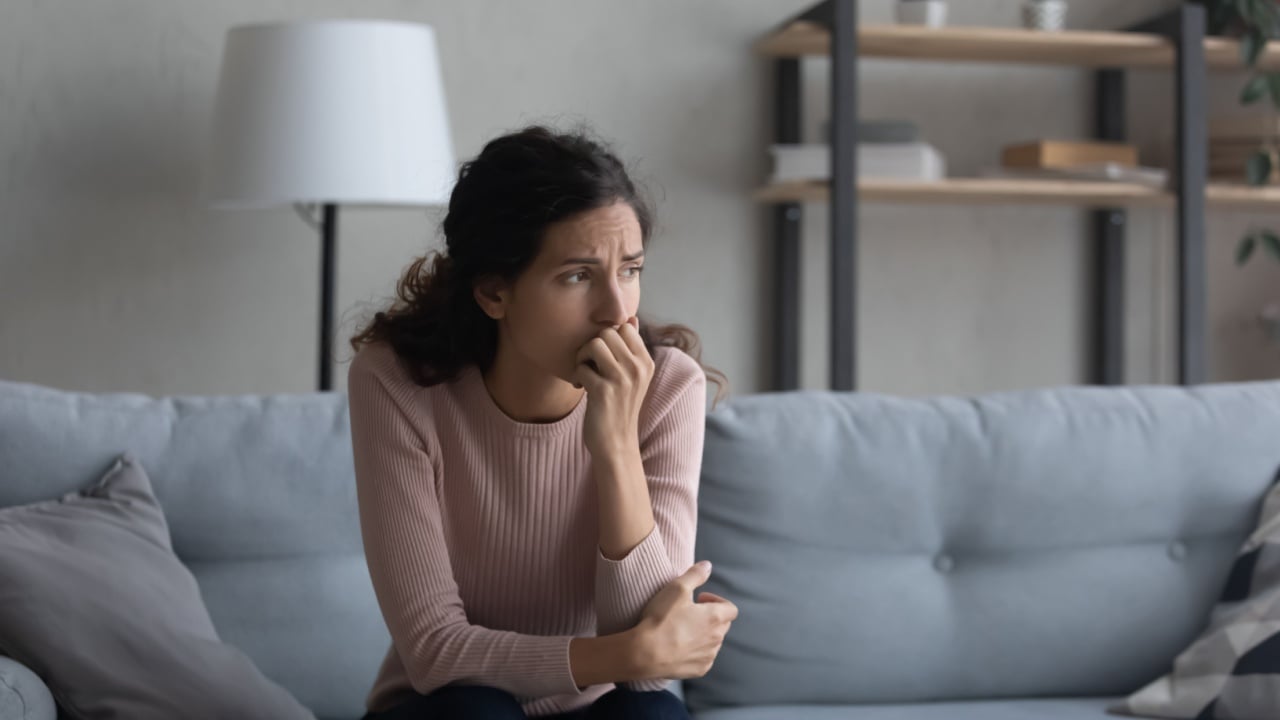 Sad young Caucasian woman sit on couch at home look in distance mourning yearning, unhappy upset female thinking suffering from relationships problems