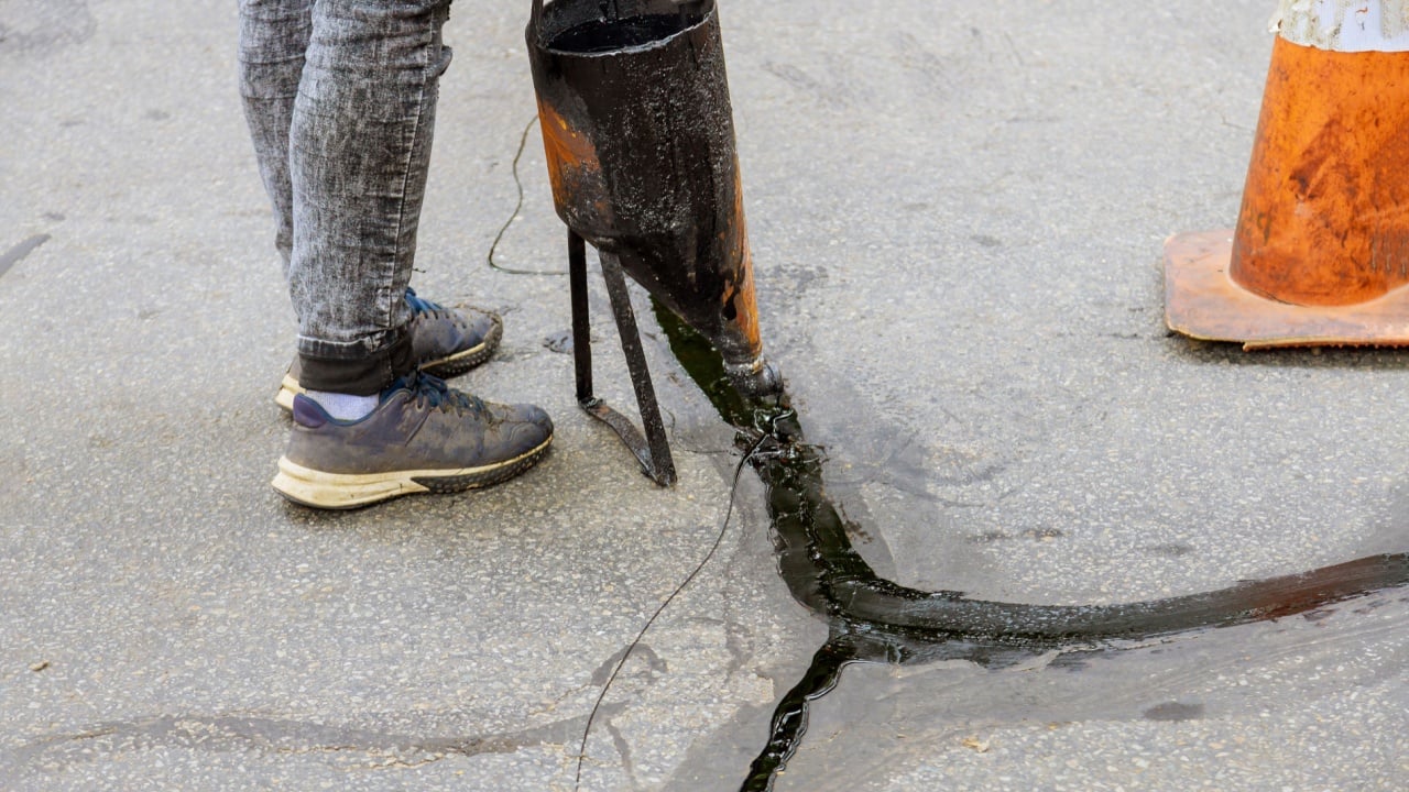 Man sealing asphalt driveway with filled cracks sealcoating selective focus
