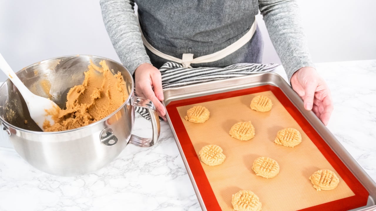 Placing a peanut butter cookie dough on silicone mats for baking.