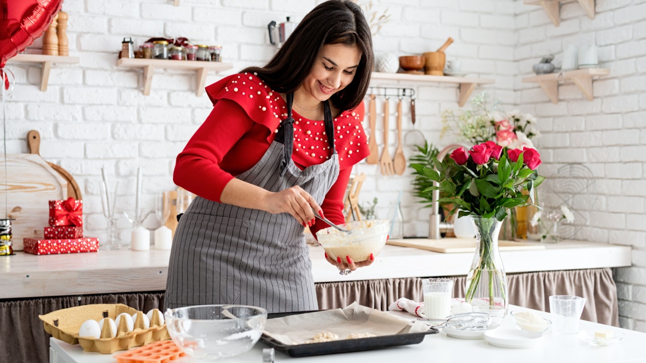Woman in red dress and gray apron making valentine cookies at the kitchen