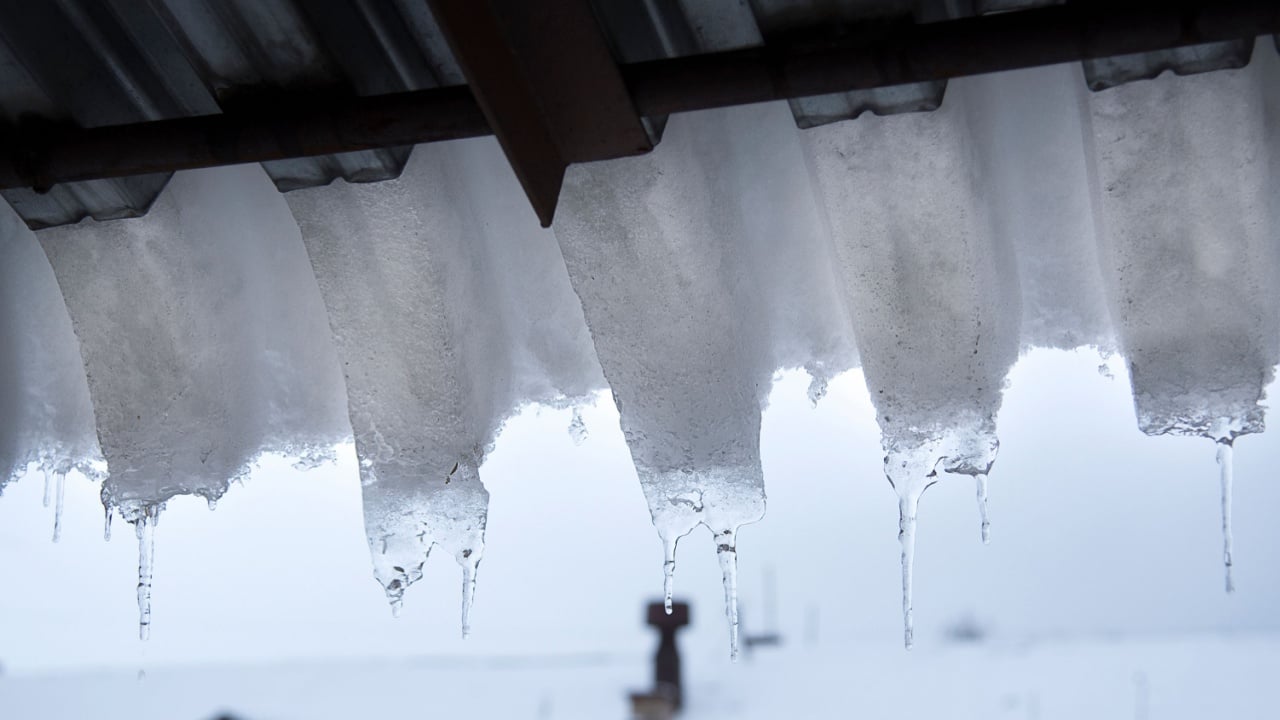 Ice and snow covers roof building, dangerous ice dams hanging from roof. Danger and safety concept. Selective focus