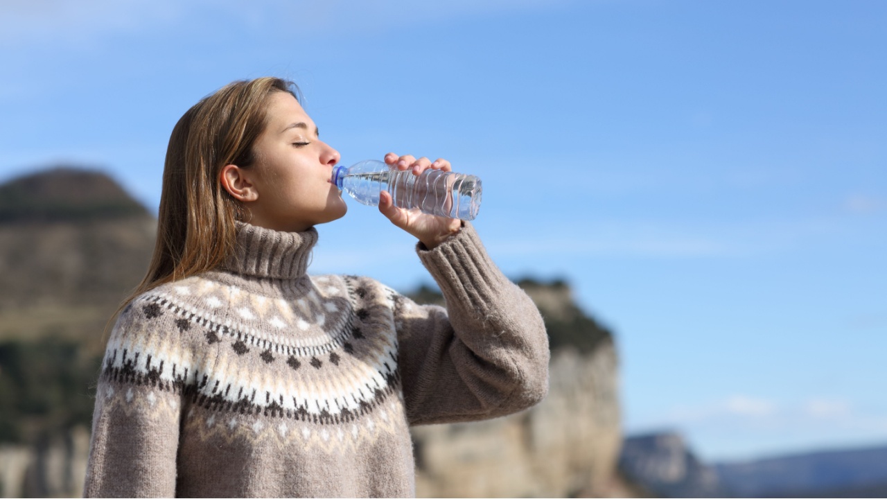 Side view portrait of a woman drinking water from plastic bottle in winter in the mountain