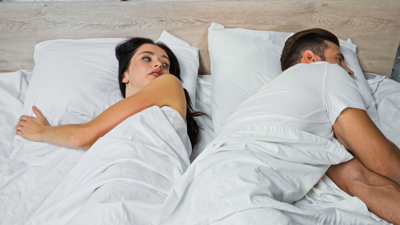brunette woman looking at boyfriend lying nearby in bed