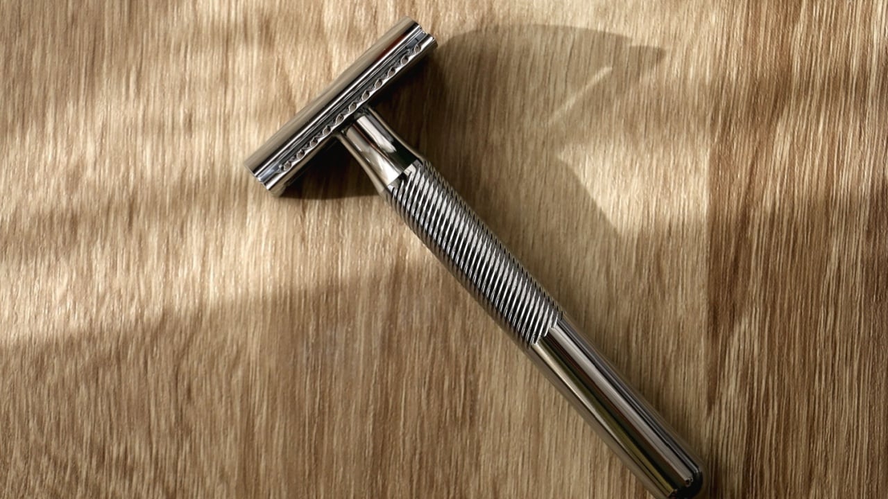Reusable metal safety razor on wooden background. Top view.