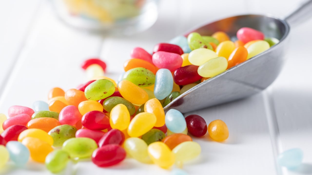 Sweet colorful jelly beans in scoop on white table.