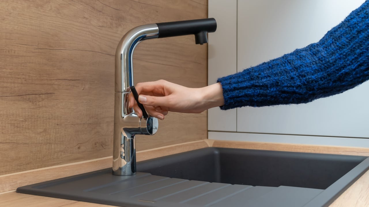 Woman's hand in a blue sweater opens a silver faucet or water tap with a graphite stone sink in the kitchen close up