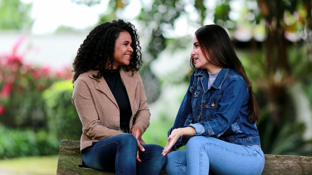 Two diverse girls talking outside together, real life laugh. Female friends bonding chatting together