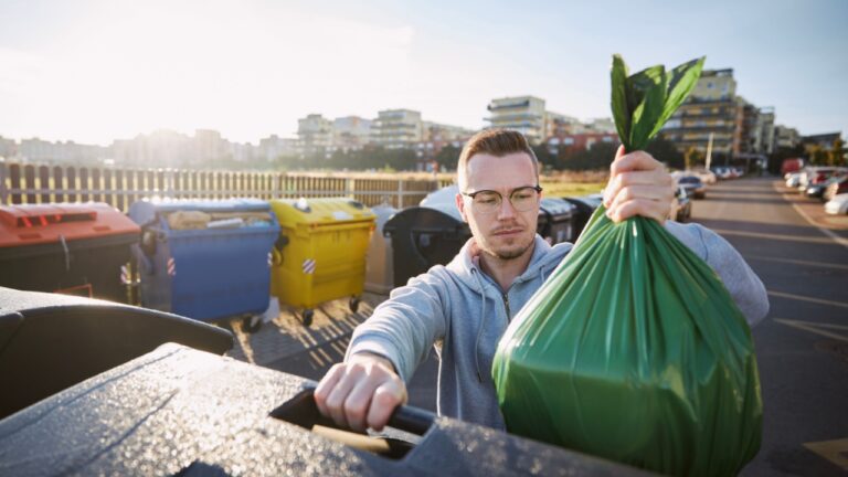 Man walking with rubbish. Front view of person throwing plastic bag to garbage can on city street.