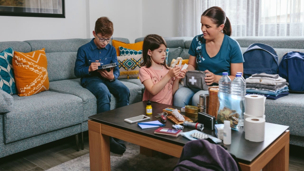 Mother preparing emergency backpack with her children in the living room