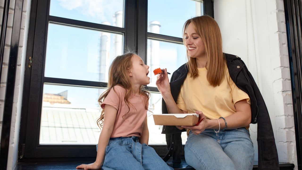 Beautiful caucasian mom and daughter eating rolls and sushi at family lunch at home. Delivery food. Traditional japanese food.