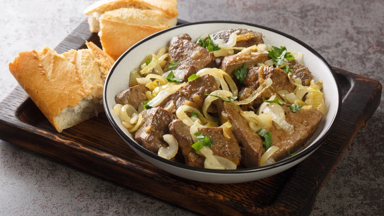Homemade food fried beef liver with onions and herbs close-up in a plate and bread on a wooden tray on the table. horizontal