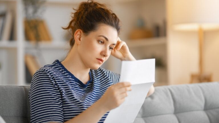 Woman, sitting on the sofa with a paper receipt in her hands, thinking about family budget.