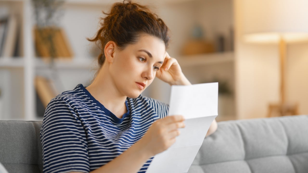 Woman, sitting on the sofa with a paper receipt in her hands, thinking about family budget.