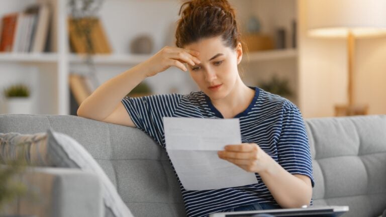 Woman, sitting on the sofa with a paper receipt in her hands, thinking about family budget.