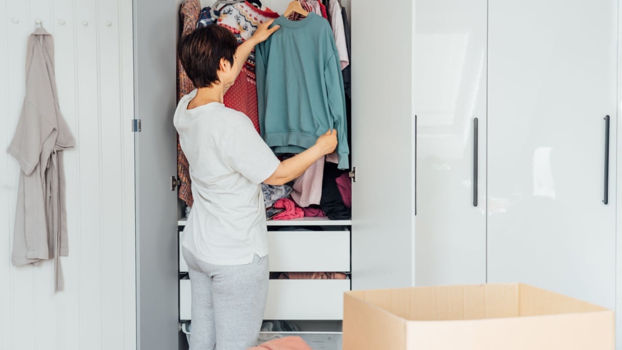 Woman selecting clothes from her wardrobe for donating to a Charity shop. Decluttering, Sorting seasonal clothes and Cleaning Up. Reuse, second-hand concept. Conscious consumer, sustainable lifestyle.