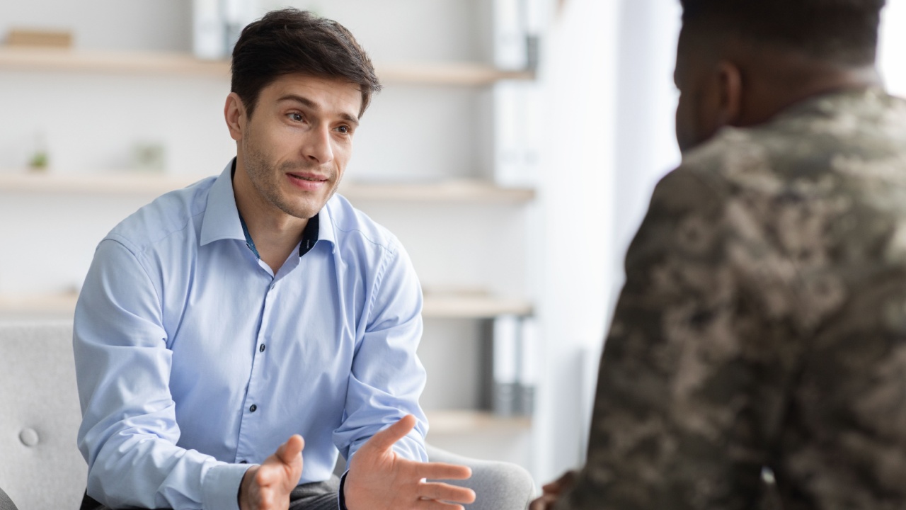 Friendly handsome young man in formal outfit doctor having conversation with black soldier, male psychologist having therapy session with african american veteran, helping with PTSD