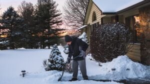 Senior man shoveling his driveway after snowfall in Midwest at sunset