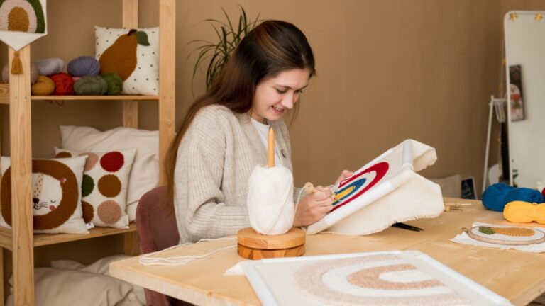 Young woman pushing the punchneedle straight down into the foundation fabric in workshop. Female embroidering handmade picture rainbow on canvas. Punch needle embroidery for beginners