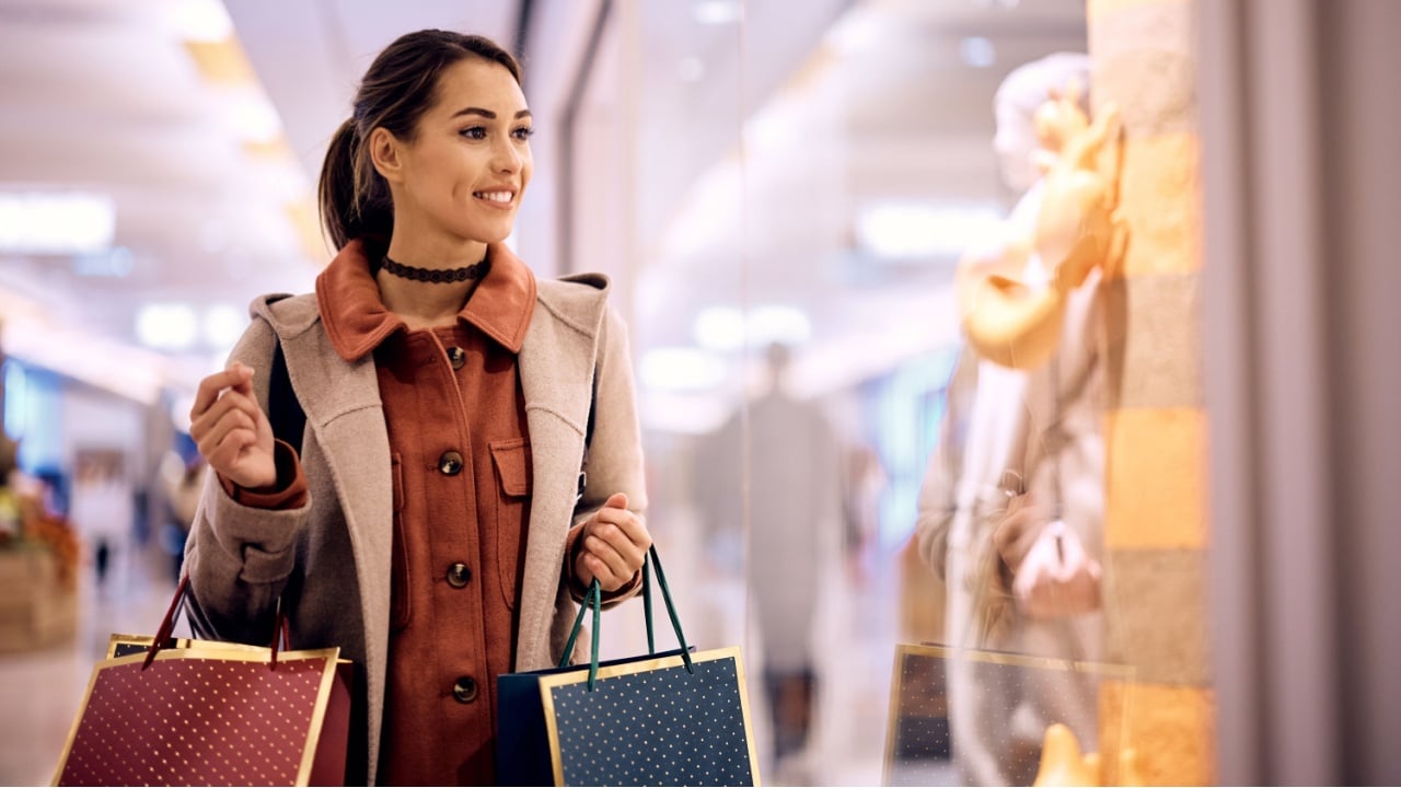 Smiling woman with shopping bags looking at store windows while walking through the mall.
