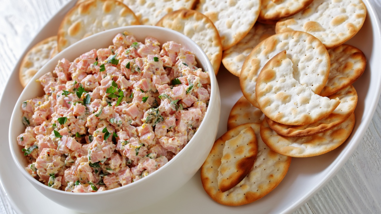 close-up of classic ham salad spread with creole mustard and mayonnaise dressing in white bowl on white plate with crackers, landscape view
