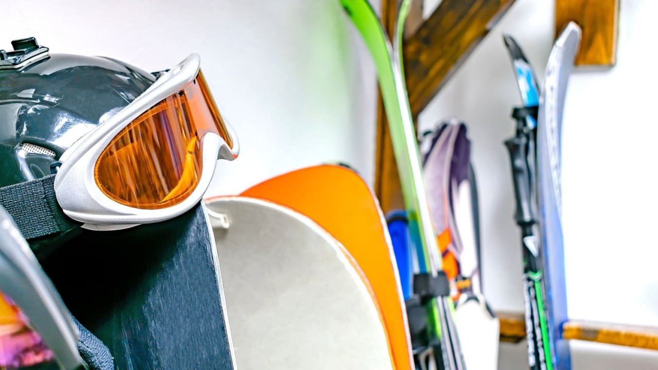 Helmet, ski mask, ski hanged on customized wooden wall mount at warehouse for seasonal storage at ski resort. Extreme winter sport equipment handling at home