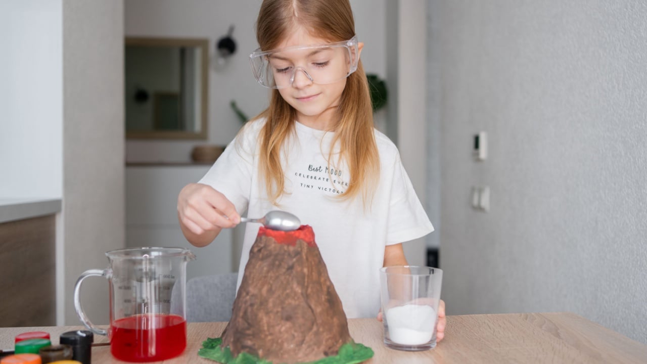 Kid science experiment of volcano or baking soda and vinegar volcano eruption for kid.Girl with eyeglasses pouring baking soda, mixed and poring vinegar for volcano labs.