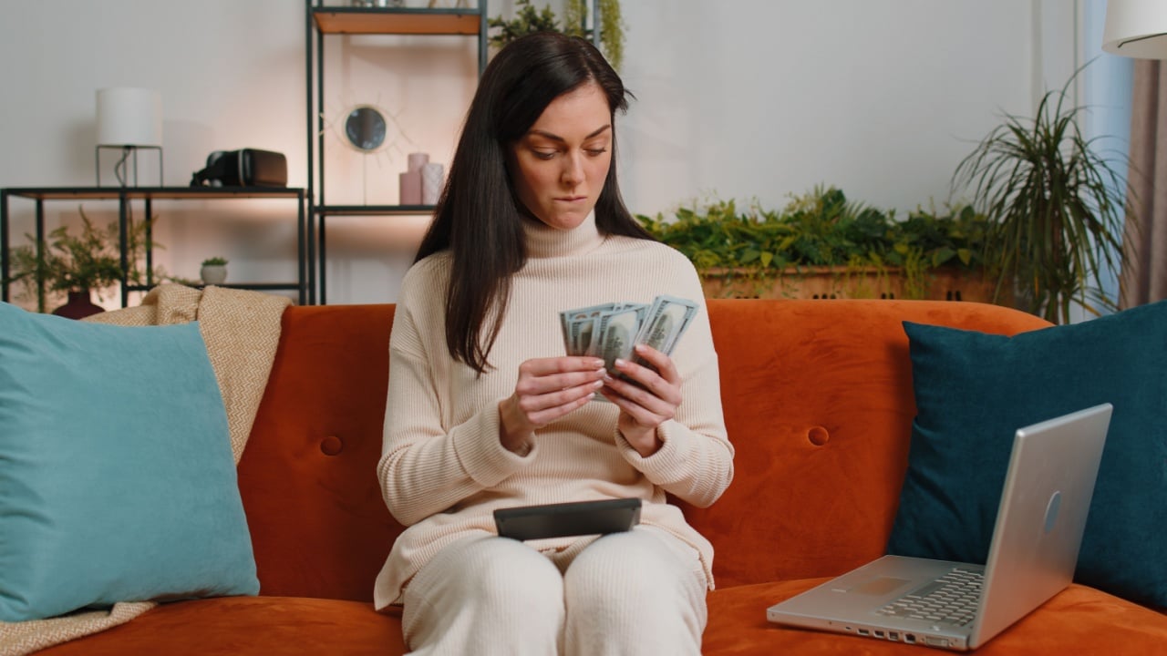 Planning budget. Rich brunette woman counting money cash use calculator and calculate domestic bills at home room. Girl satisfied of income earnings, win, saves money for planned vacation, gifts