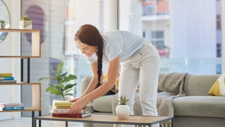 Woman, cleaning and house with books in lounge, table and organize for housekeeping, tidy and order. Happy cleaner girl, book stack and living room for clean home, neat apartment or flat in New York