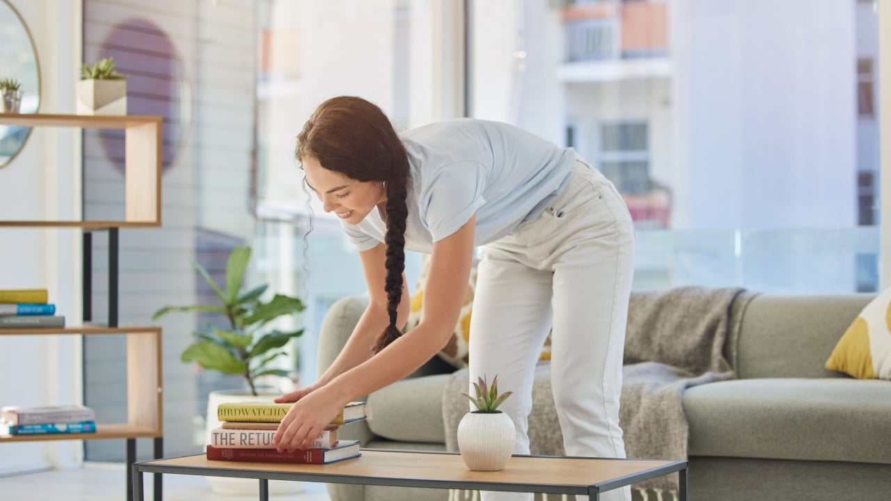Woman, cleaning and house with books in lounge, table and organize for housekeeping, tidy and order. Happy cleaner girl, book stack and living room for clean home, neat apartment or flat in New York