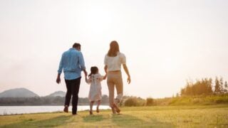 Happy family in the park sunset light. family on weekend running together in the meadow with river Parents hold the child hands.health life insurance plan concept.