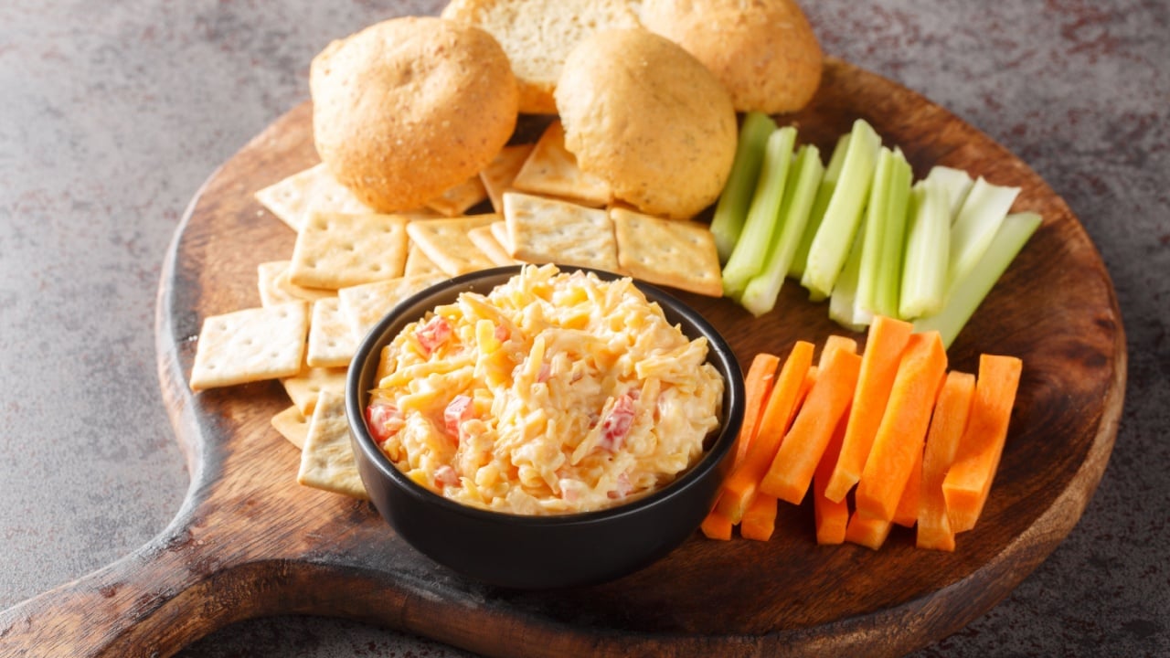 Homemade Pimento Cheese Dip with carrots, celery and crackers, side view closeup on the wooden board on the table. Horizontal