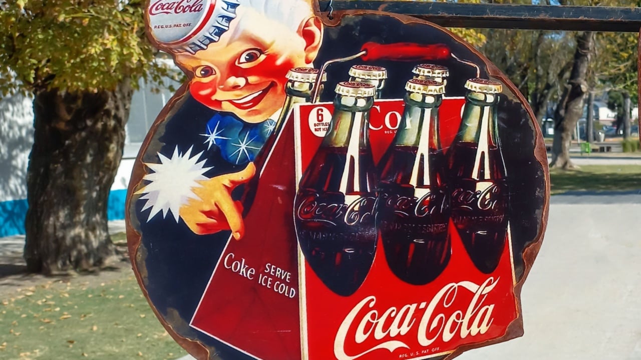 AVELLANEDA, AR - May 09, 2022: Old rusty tin advertisement sign logo 1940s. Sprite boy with a six bottles pack. Coke serve ice cold. Coca Cola is a famous American soft drink brand.