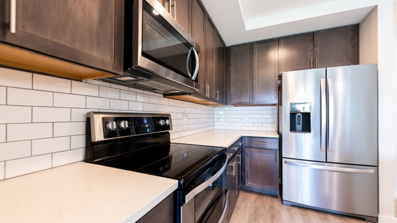 Nobody in modern luxury residential kitchen with tile backsplash quartz countertop by clean new fridge refrigerator stove oven and microwave appliances cabinets