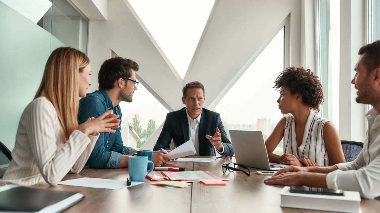 Staff meeting. Serious mature man discussing new project with his multicultural team while sitting at the office table