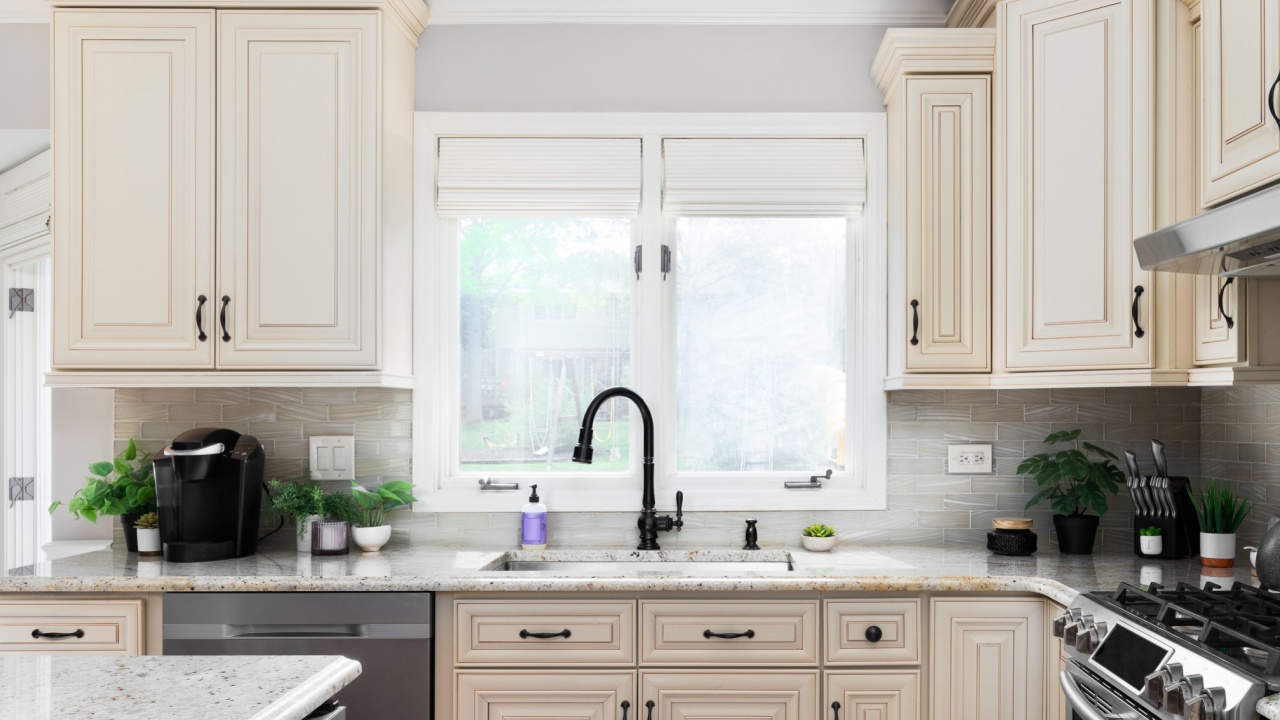 A kitchen detail with light brown cabinets, a black faucet, and decorations on the marble countertop.