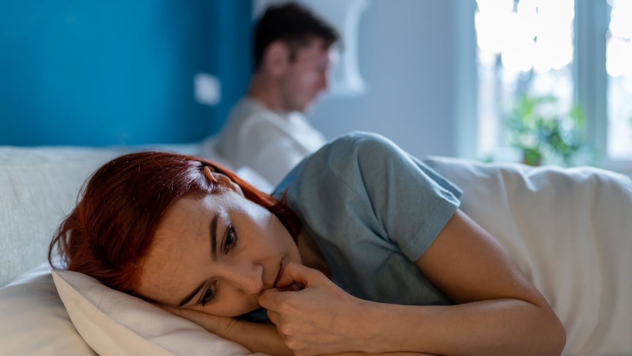Upset wife lies with her back to husband. Frustration, unhappiness, pain, resentment and thoughtfulness on face of sad depressed woman lying in bed thinking. Man with disinterested look ignores woman.